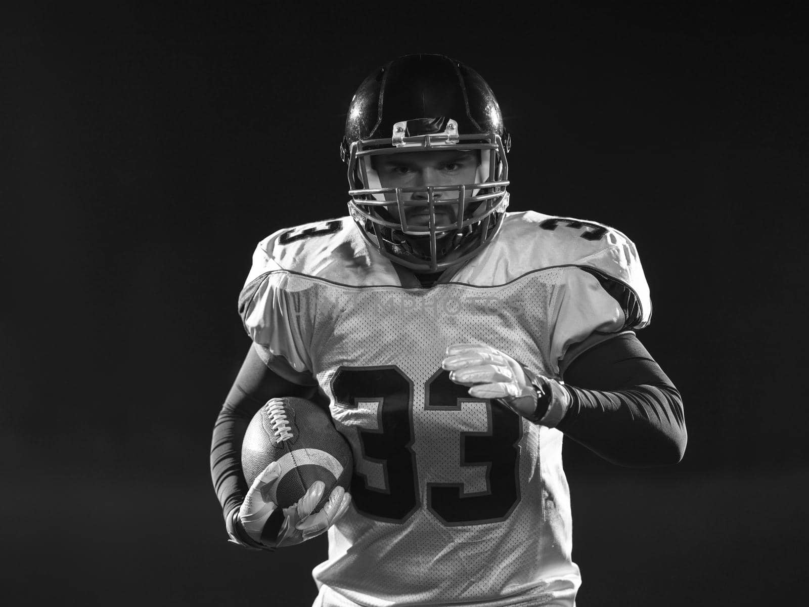 portrait of confident American football player holding ball while standing on field at night