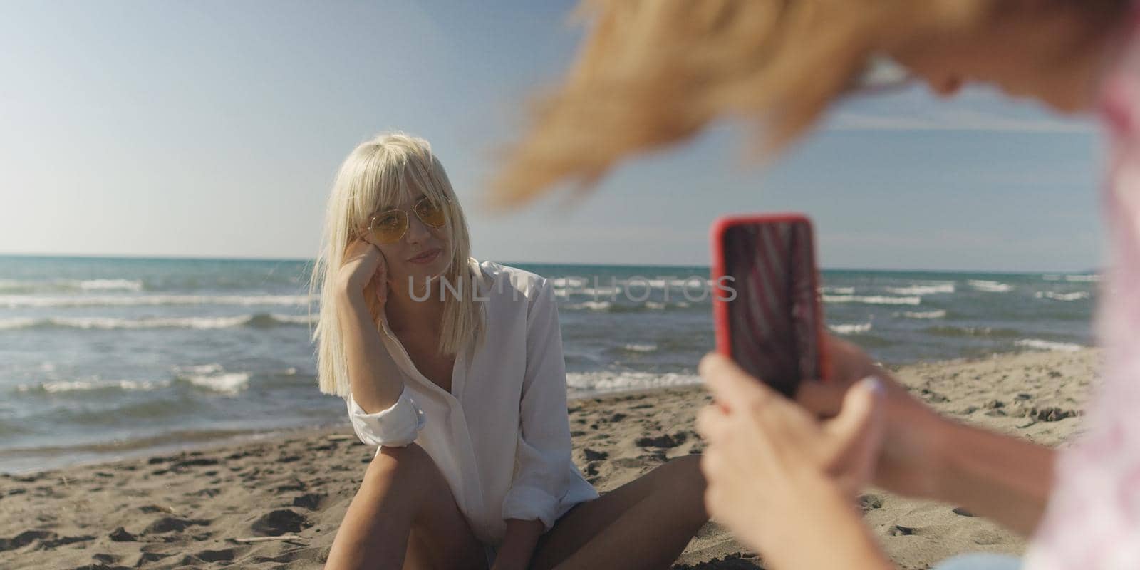 Two Girl Friends Taking Photo with Smartphone On Empty Beach during autumn day