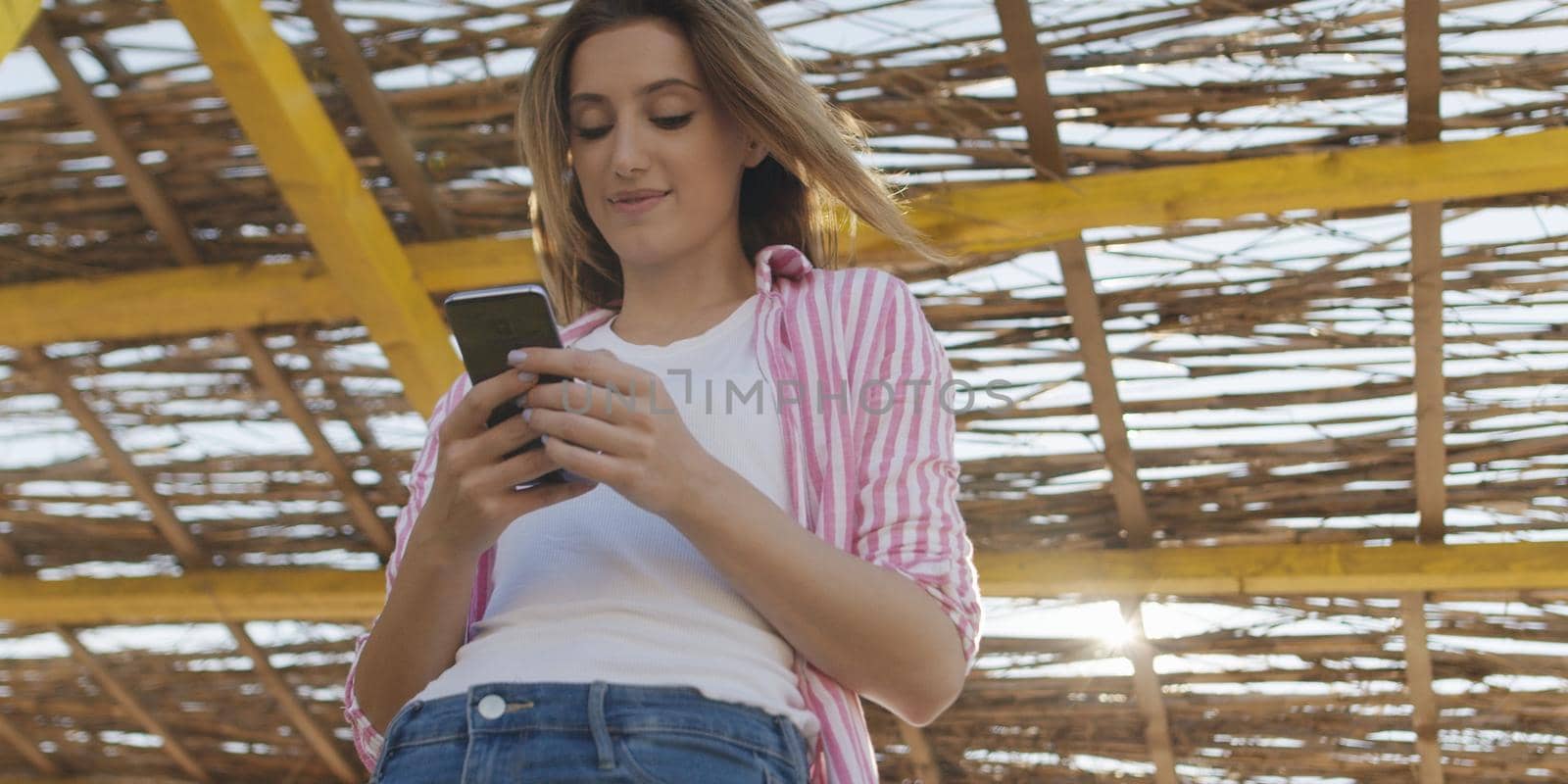 young woman using mobile cell smart phone app at beach during sunset on autumn day