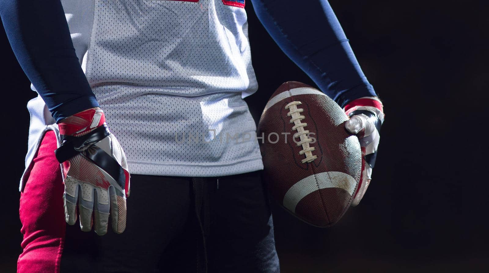 portrait of confident American football player holding ball while standing on field at night