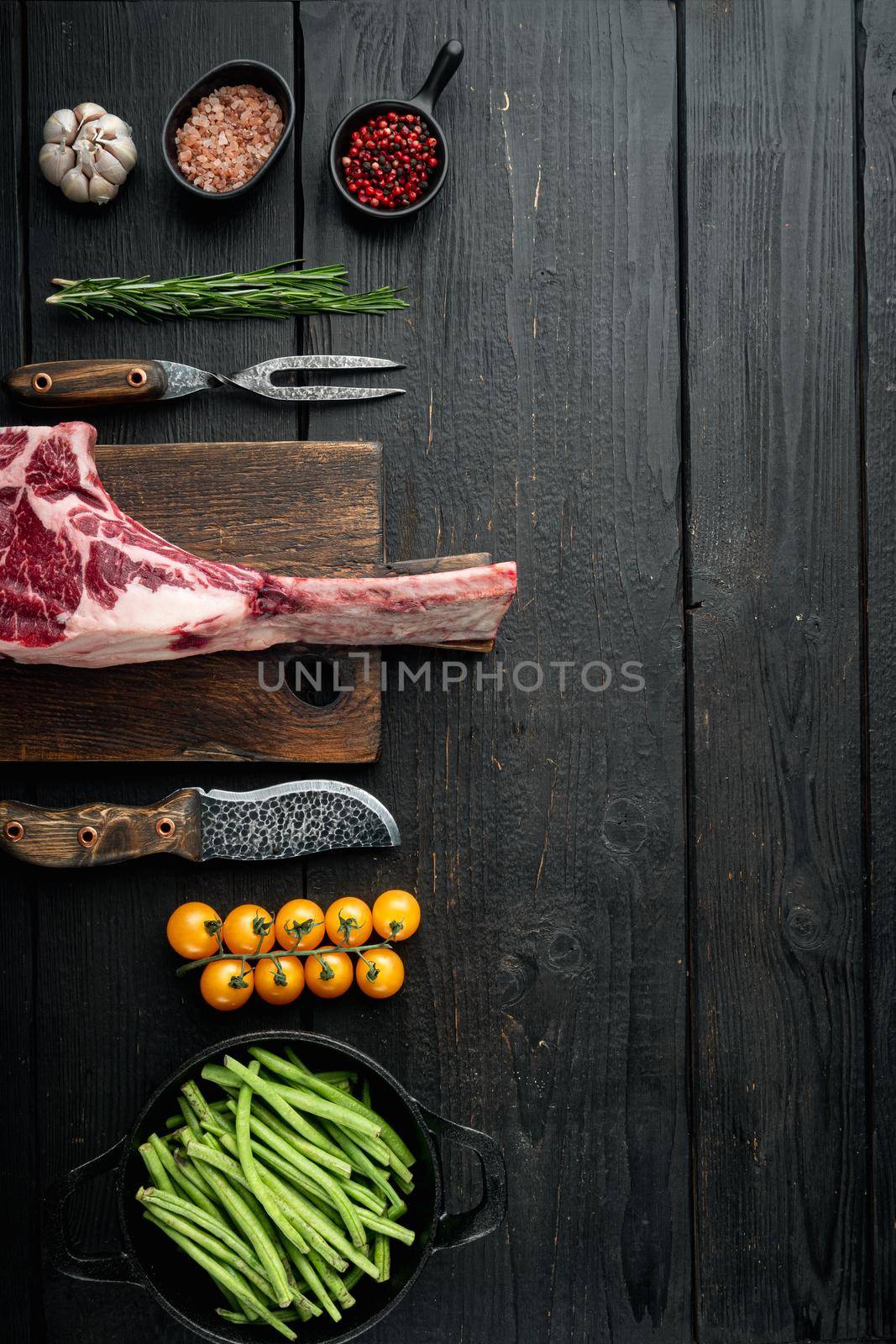 Cooking meat background. Raw tomahawk steak, with spices and herbs for cooking set, with grill ingredients, on black wooden table background, top view flat lay, with copy space for text