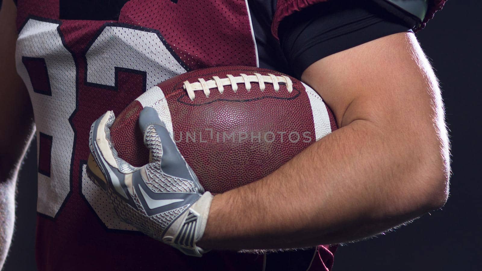 portrait of confident American football players holding ball while standing on field at night