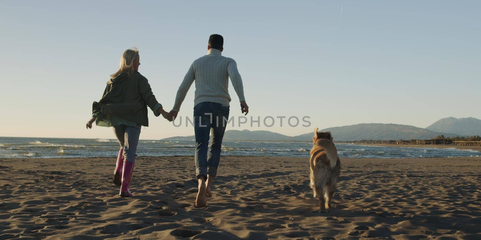 Couple Running On The Beach Holding Their Hands with dog On autmun day