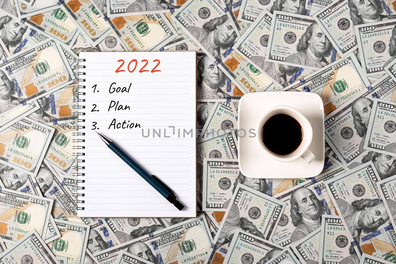 2022, GOAL, PLAN and ACTION. Notepad, pen and a cup of black coffee isolated on money background. Notepad with copy space. Office, business, discreet style.
