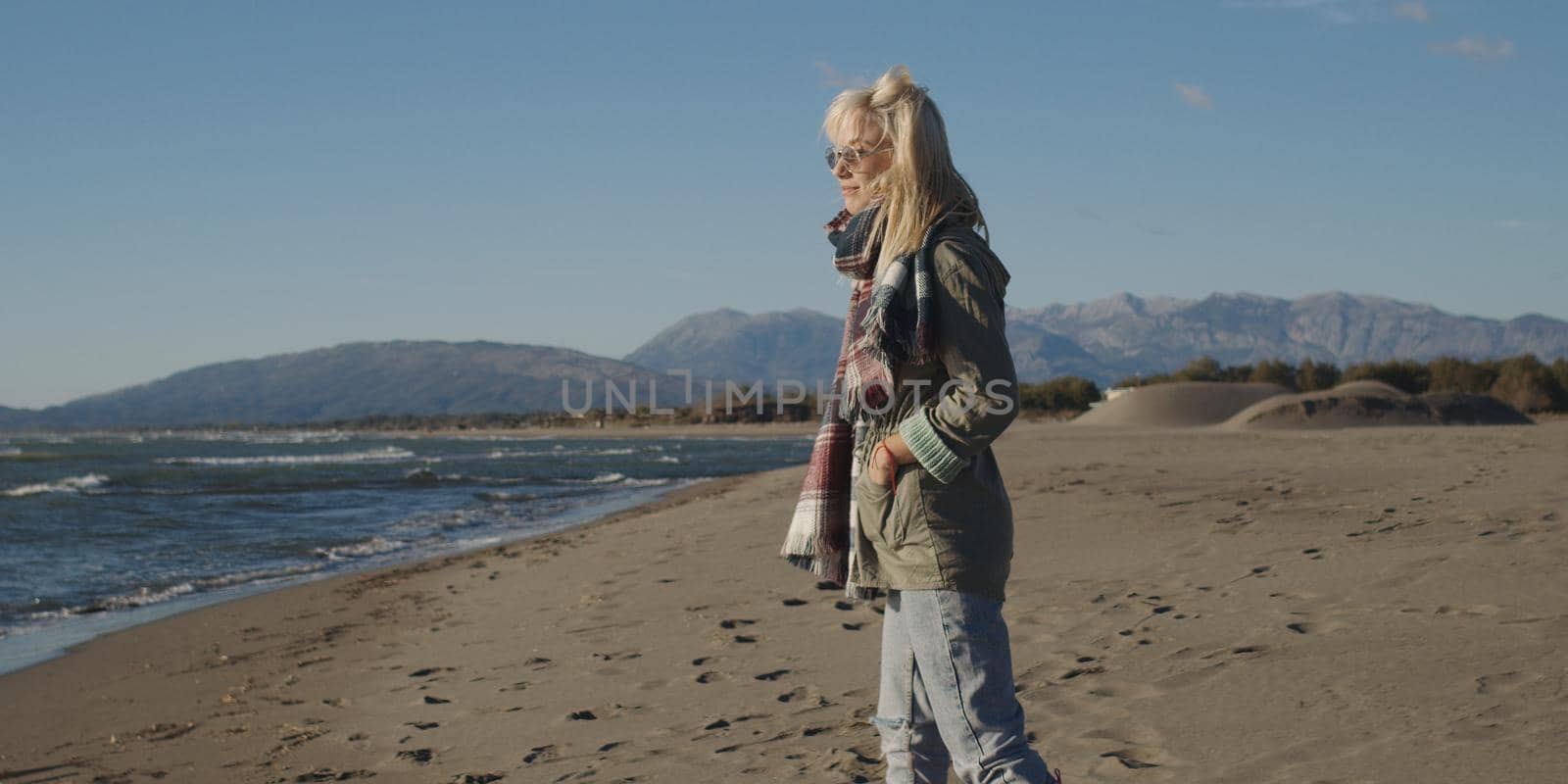 Young woman on the beach. The girl enjoying the warm autumn day. Portrait of beautiful girl near the water