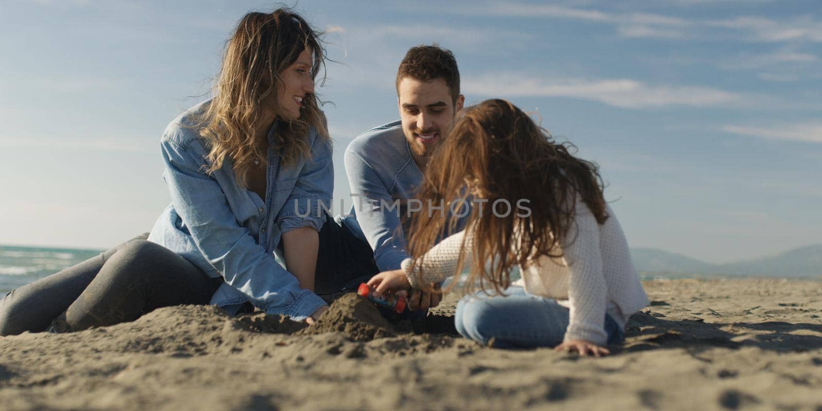 Family with kids resting and having fun at beach during autumn day