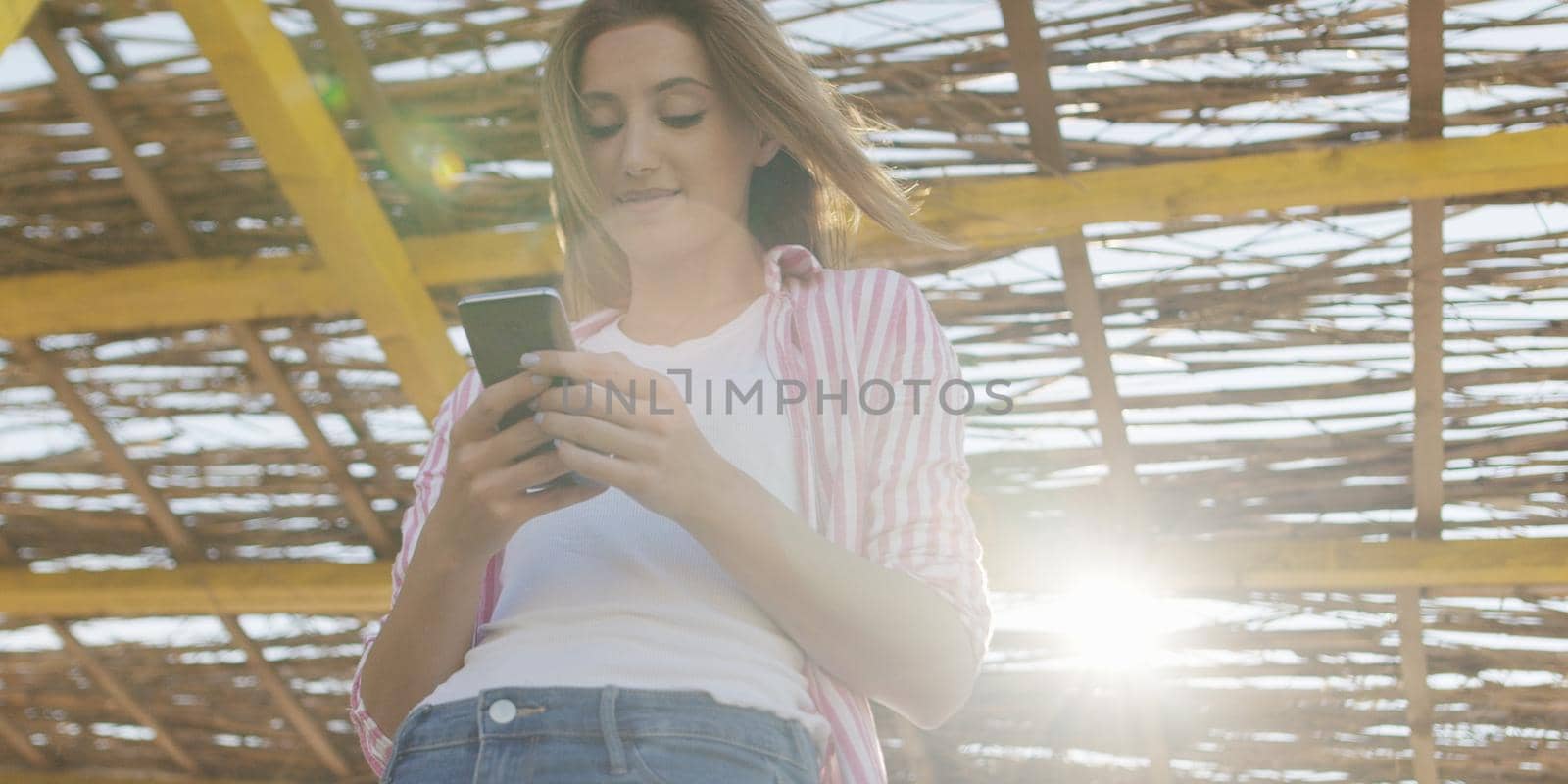 young woman using mobile cell smart phone app at beach during sunset on autumn day