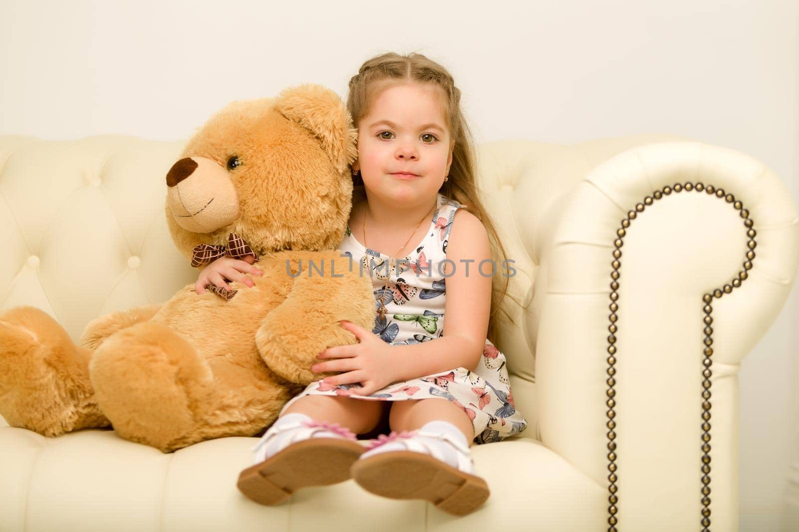 Beautiful little girl on sofa hugging teddy bear. The concept of a happy childhood, game in the family.