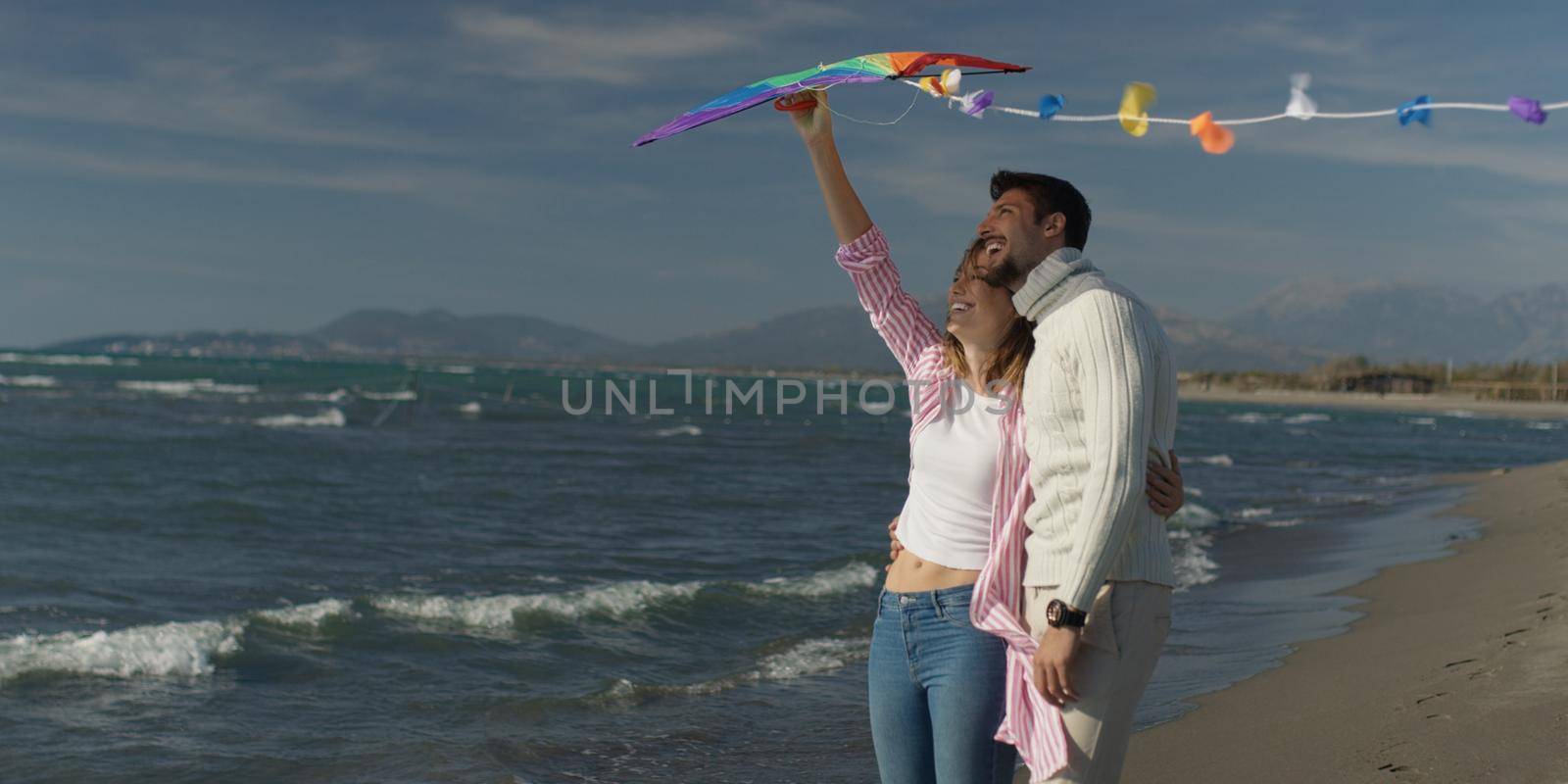 Happy couple having fun with kite on beach by dotshock