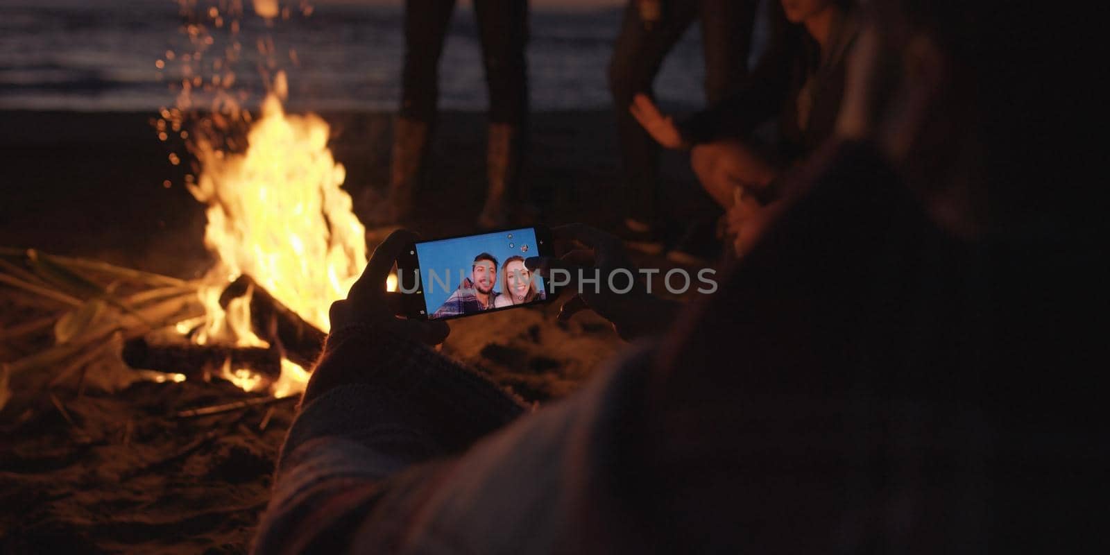 Couple taking photos beside campfire on beach by dotshock