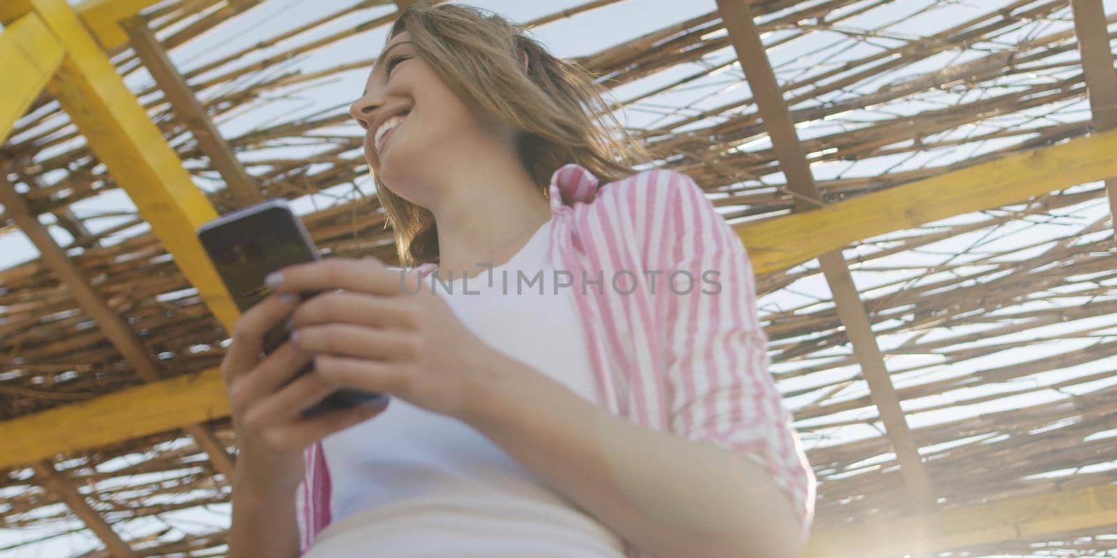 young woman using mobile cell smart phone app at beach during sunset on autumn day