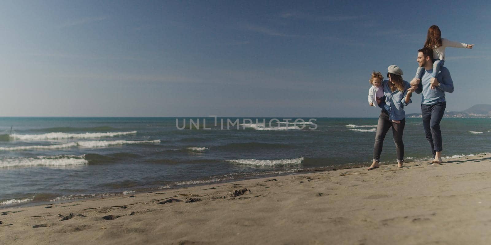 Family with kids resting and having fun at beach during autumn day