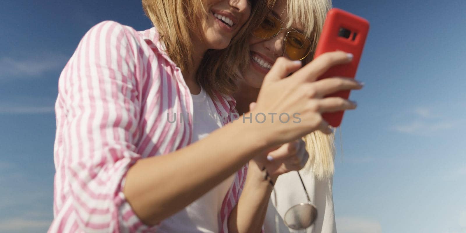 Two Girl Friends Taking Photo with Smartphone On Empty Beach during autumn day