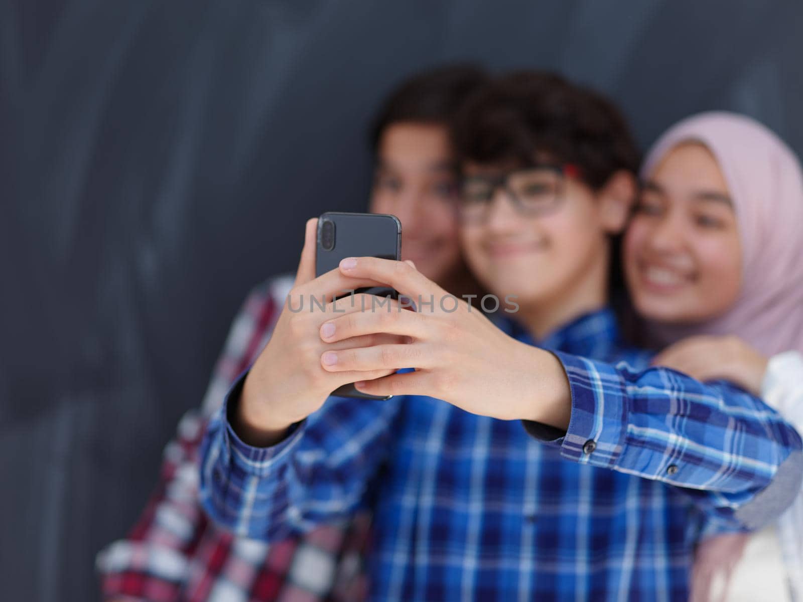 group of arab teens taking selfie photo on smart phone with black chalkboard in background