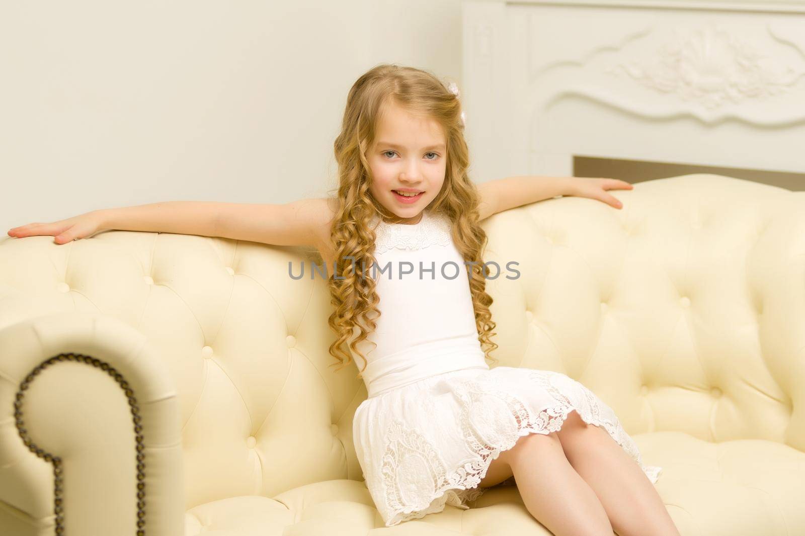 Little girl is sitting on the couch in the room. The concept of a happy childhood.