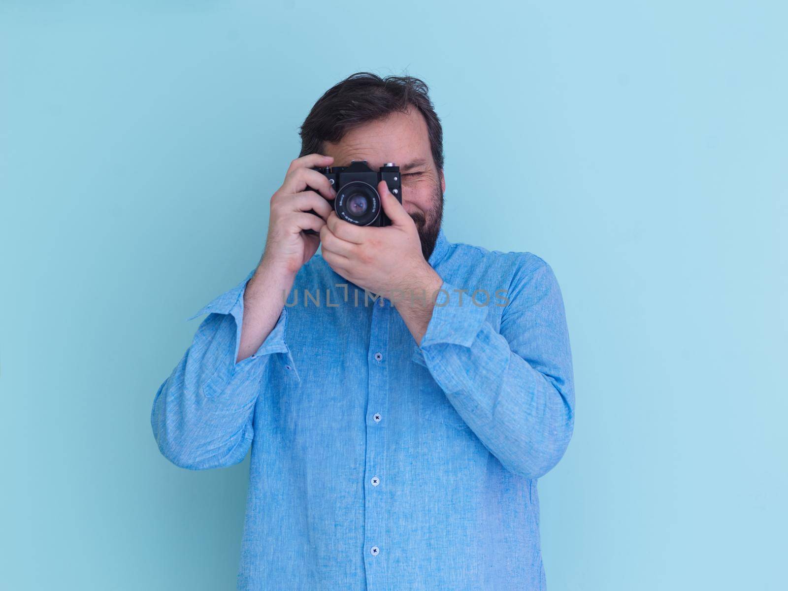Portrait of  male Photographer in blue shirt holding old analog slr art camera while standing against cyan background