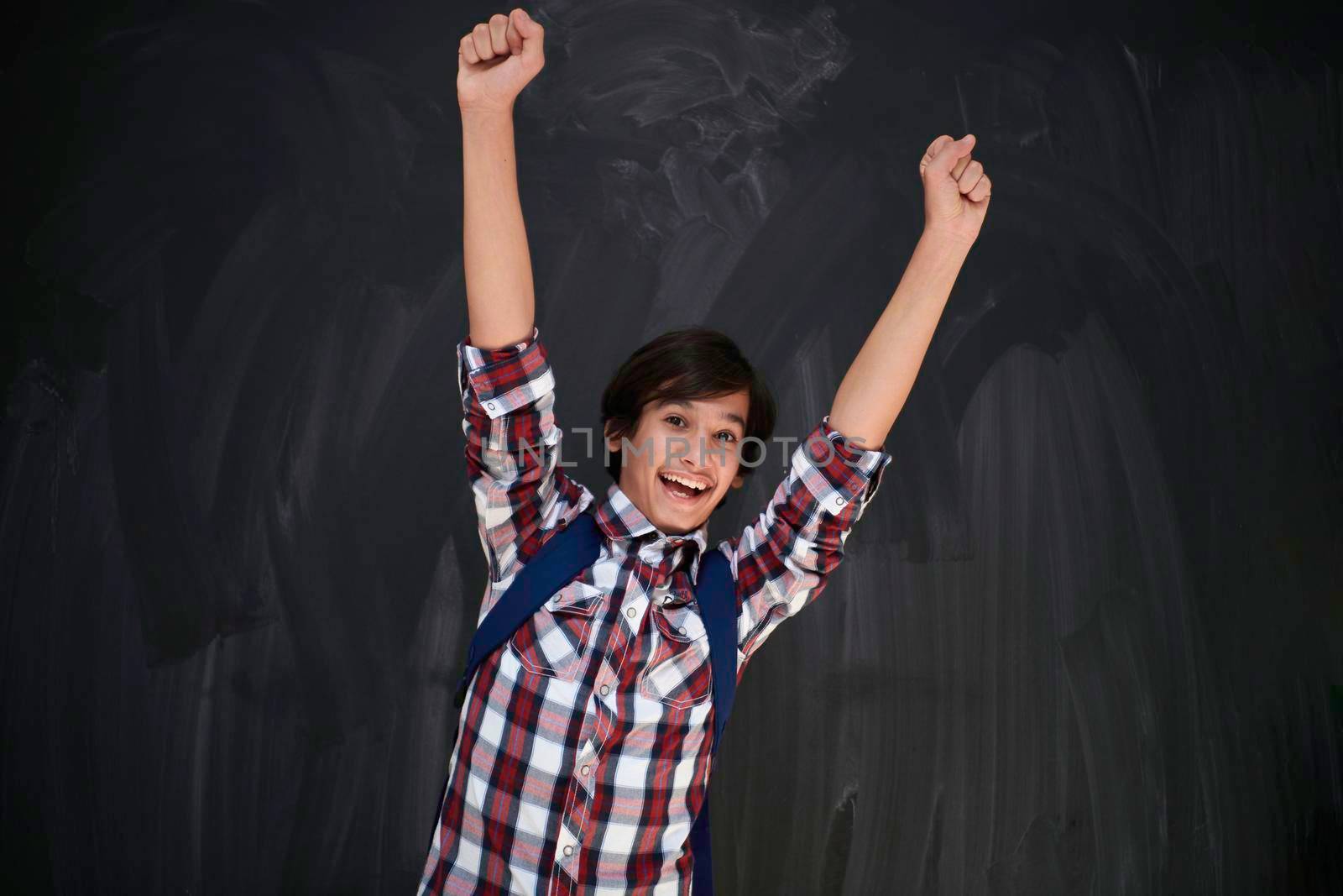 happy arab teenager celebrating wearing  backpack  casual school look against black chalkboard background