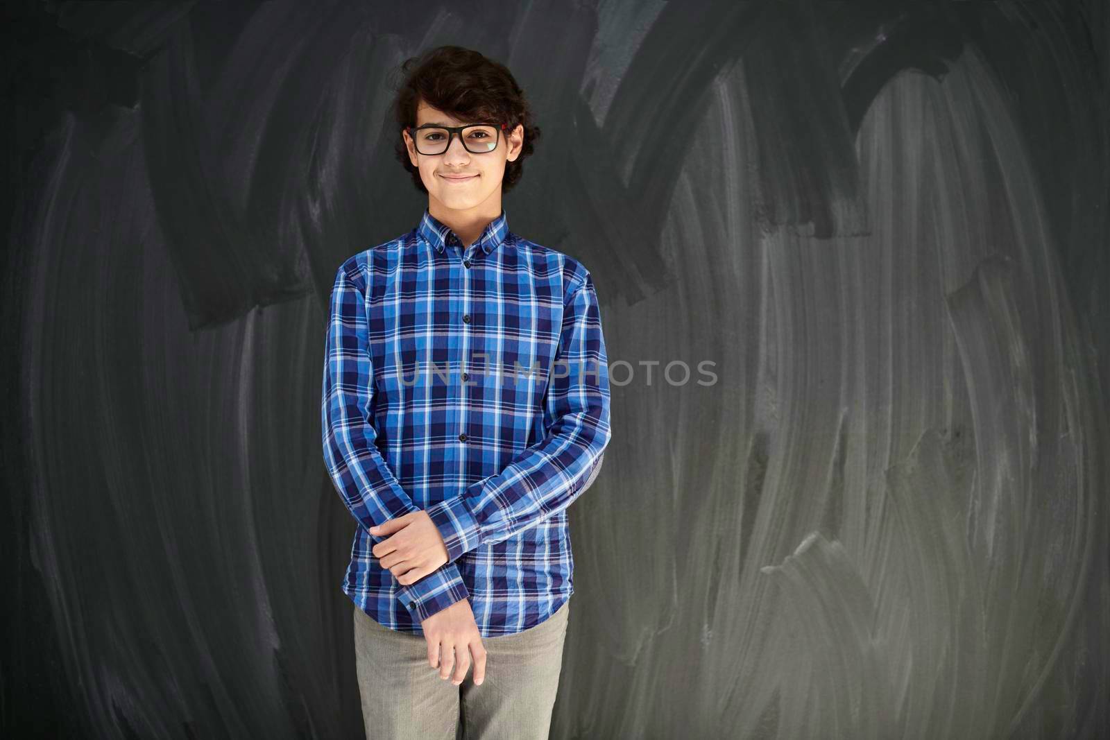 portrait  of smart looking arab teenager with glasses against black chalkboard by dotshock