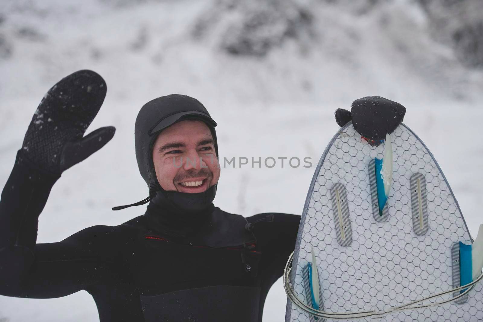 Authentic local Arctic surfer portrait holding a board after surfing in Norwegian sea. Snow capped mountain background. Winter water activities extreme sport