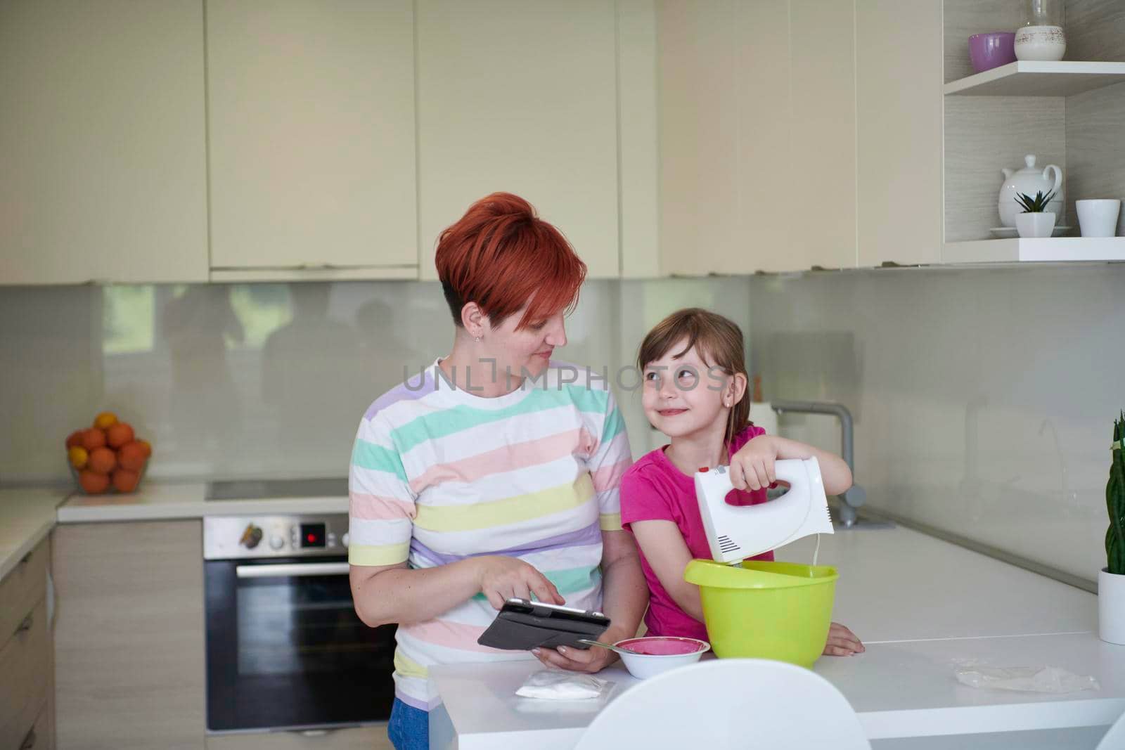 Happy family in the kitchen playing games and learning to cooking while staying at home during coronavirus covid-19 pandemic isolation. Mother and child daughter preparing the cake and cookies.