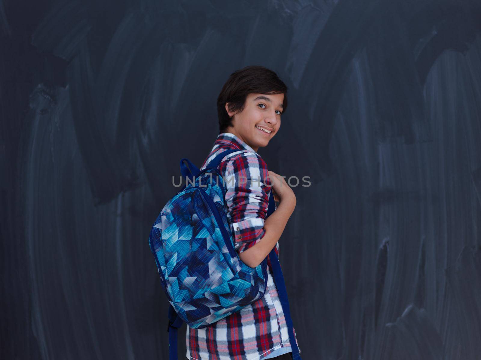 arab teenager with backpack wearing  casual school look against black chalkboard background