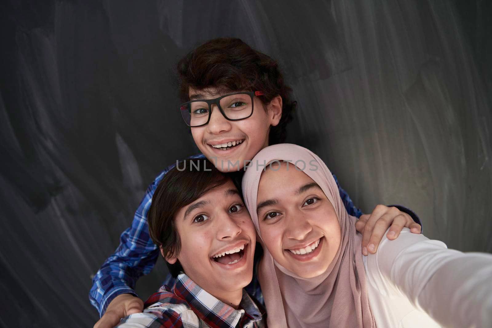 group of arab teens taking selfie photo on smart phone with black chalkboard in background