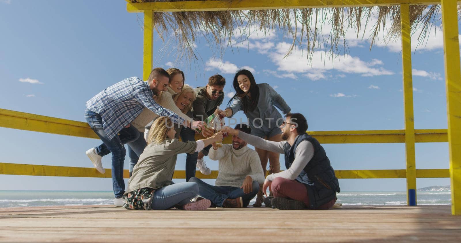 Happy Group Of Friends Hanging Out At Beach House having fun and drinking beer on autumn day