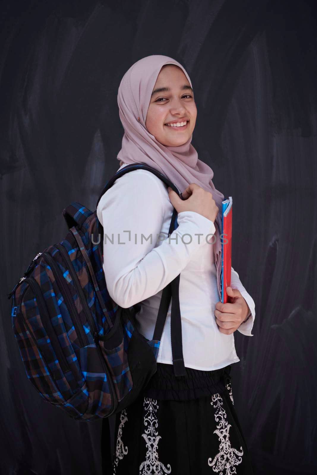 portrait of happy female middle eastern university student against black chalkboard in classroom