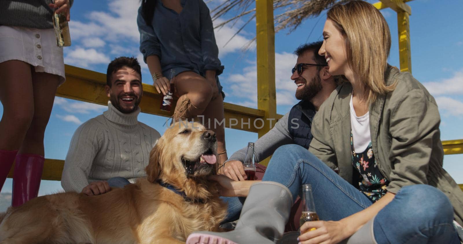 Happy Group Of Friends Hanging Out At Beach House having fun and drinking beer on autumn day