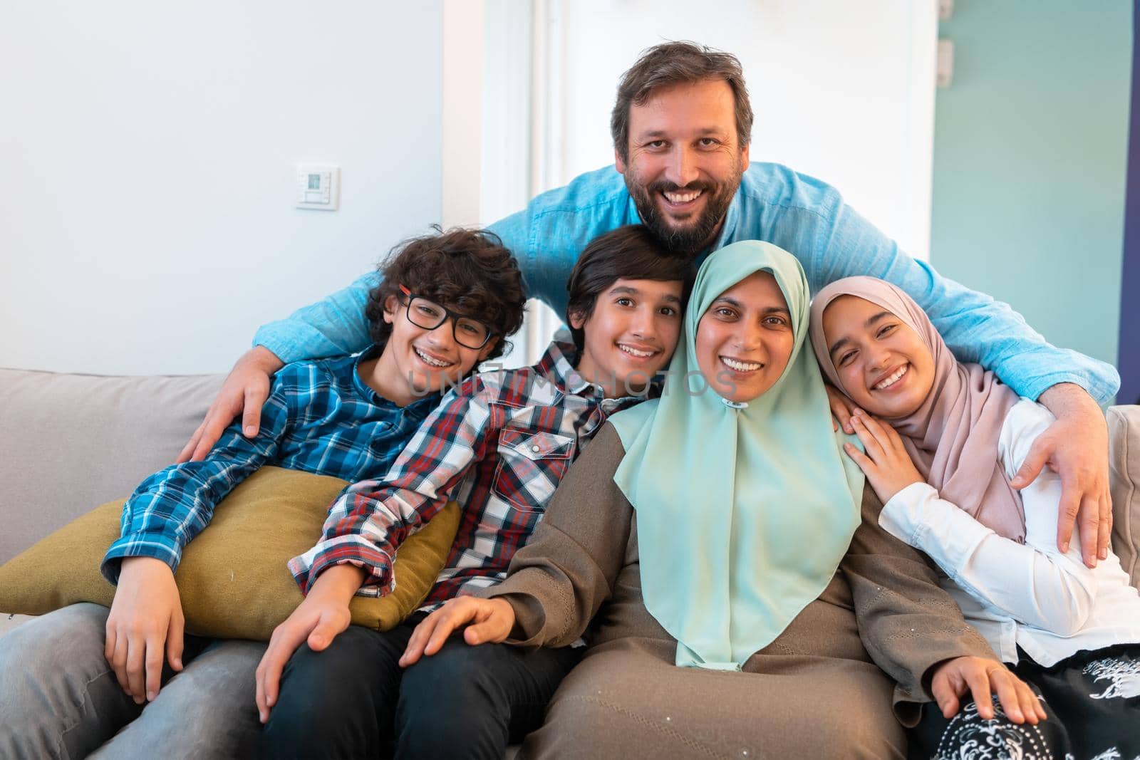 Portrait photo of an Arab Muslim family sitting on a couch in the living room of a large modern house. Selective focus. High quality photo
