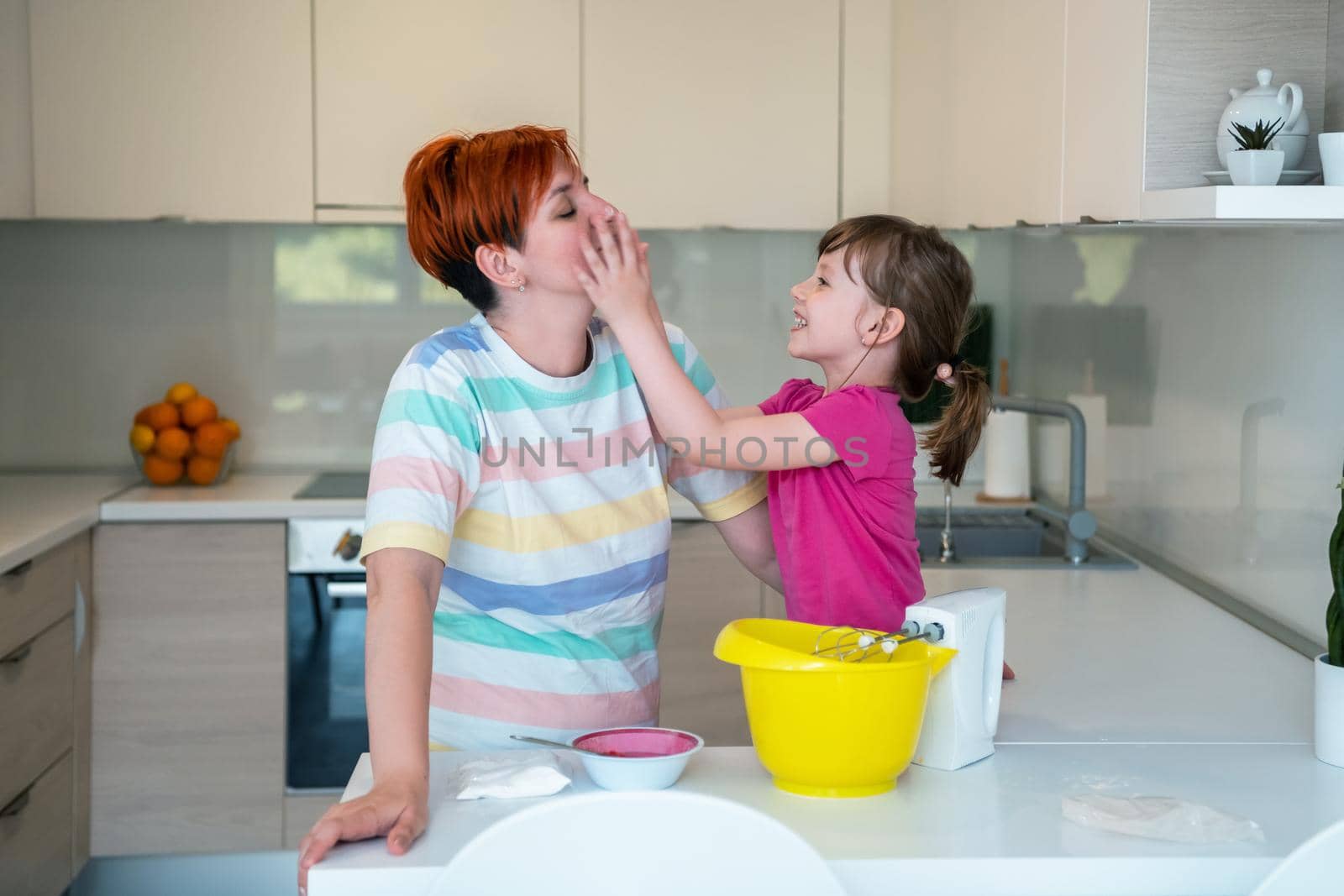 Funny little girl helper playing with dough on his hands learning to knead helps adult mom in the kitchen, happy cute baby daughter and parent mom have fun cooking cookies. by dotshock