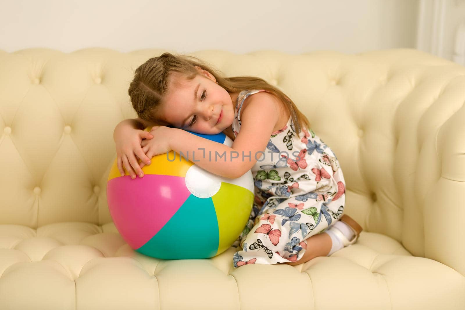 Adorable little girl playing with a ball on the sofa. Concept for family, advertising, happy childhood.