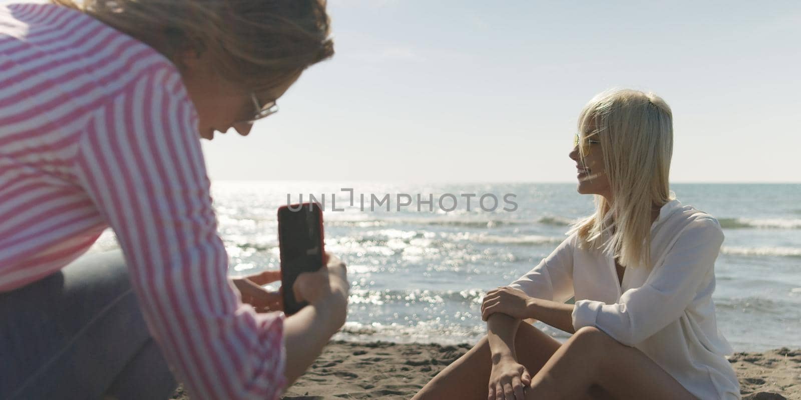 Two Girl Friends Taking Photo with Smartphone On Empty Beach during autumn day