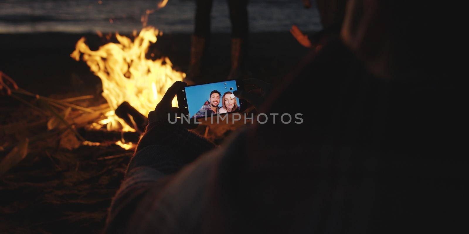 Couple taking photos beside campfire on beach by dotshock