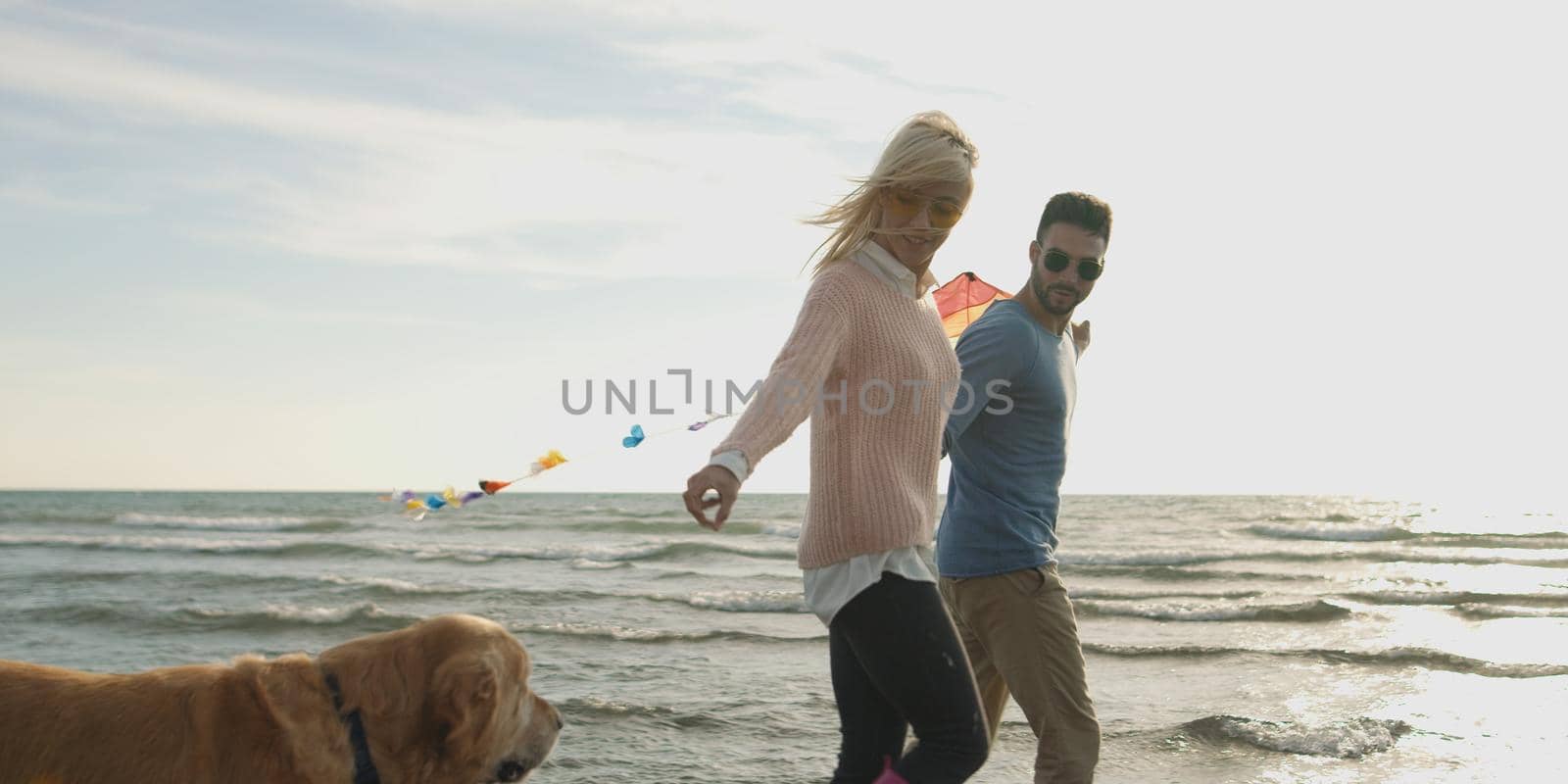 Couple Running On The Beach Holding Their Hands with dog On autmun day