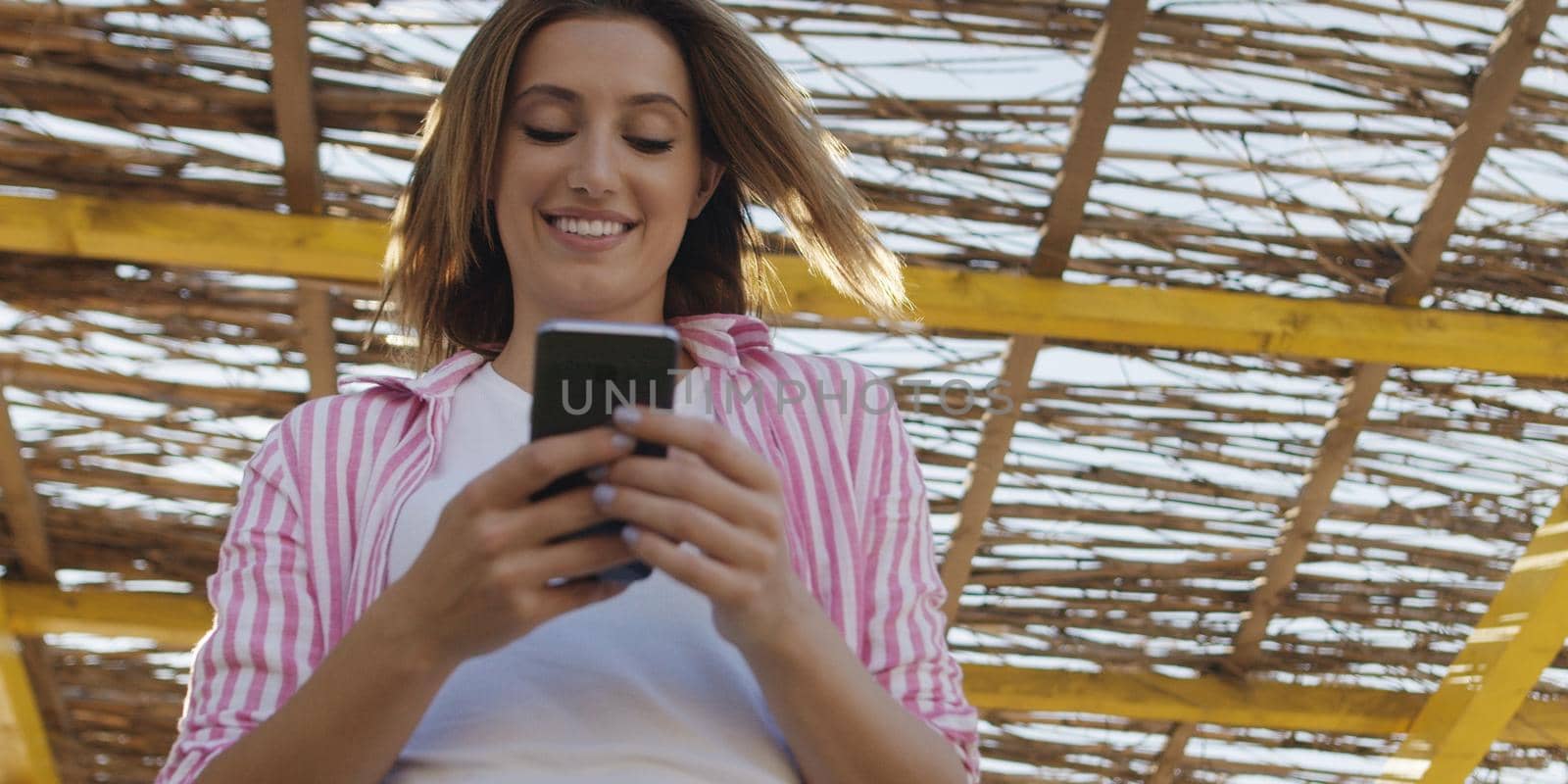 young woman using mobile cell smart phone app at beach during sunset on autumn day