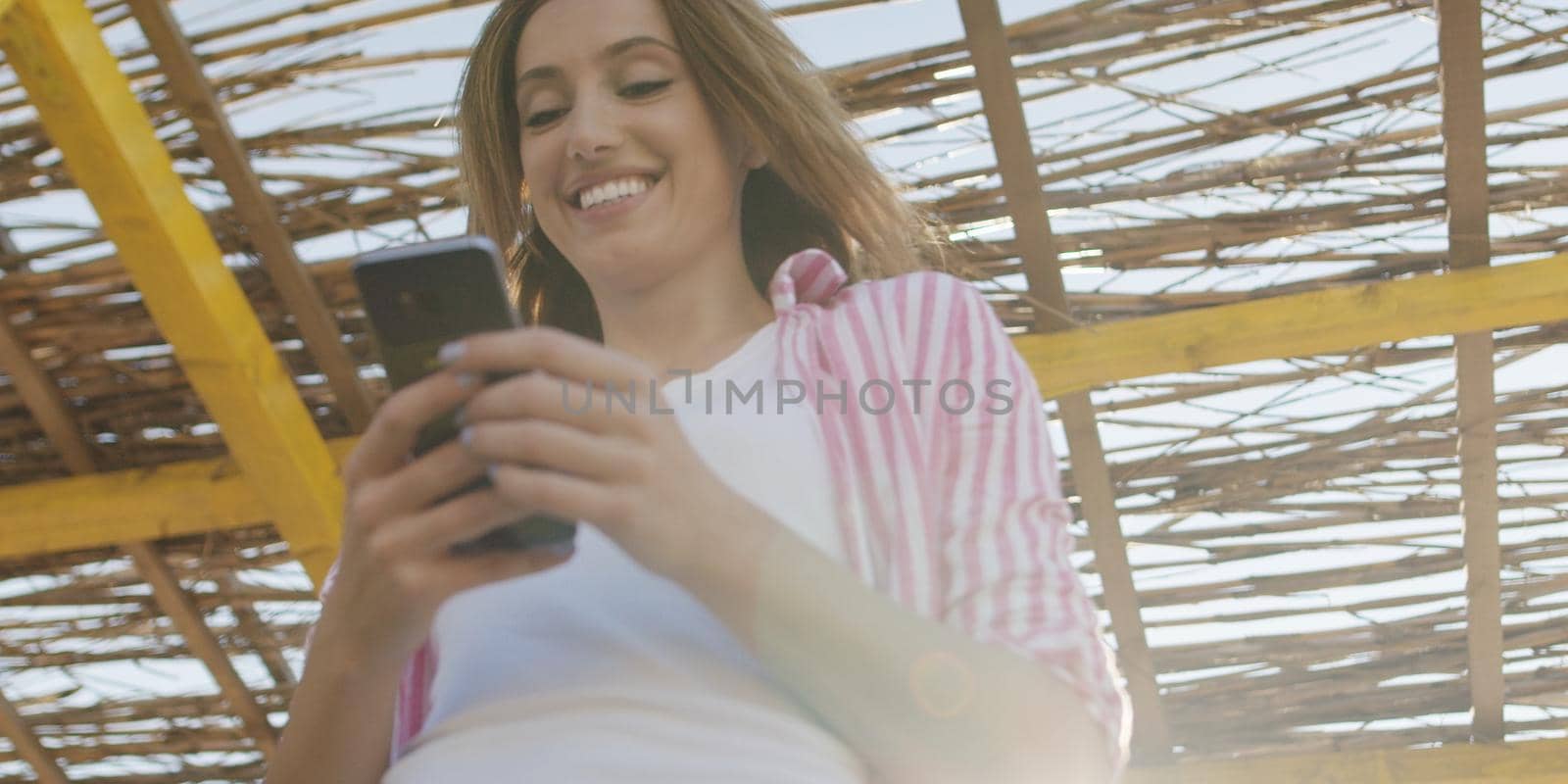 young woman using mobile cell smart phone app at beach during sunset on autumn day