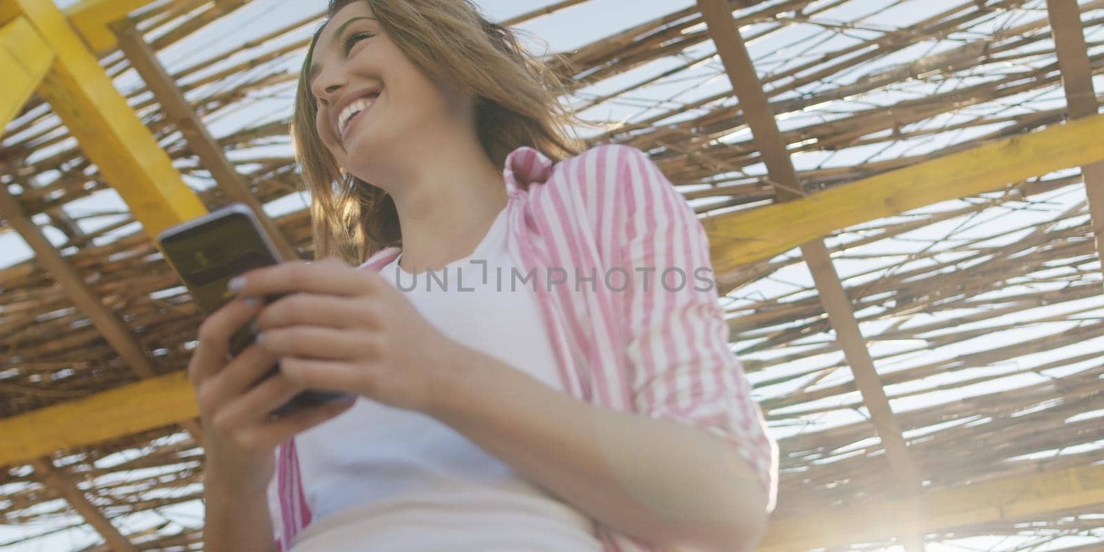 young woman using mobile cell smart phone app at beach during sunset on autumn day