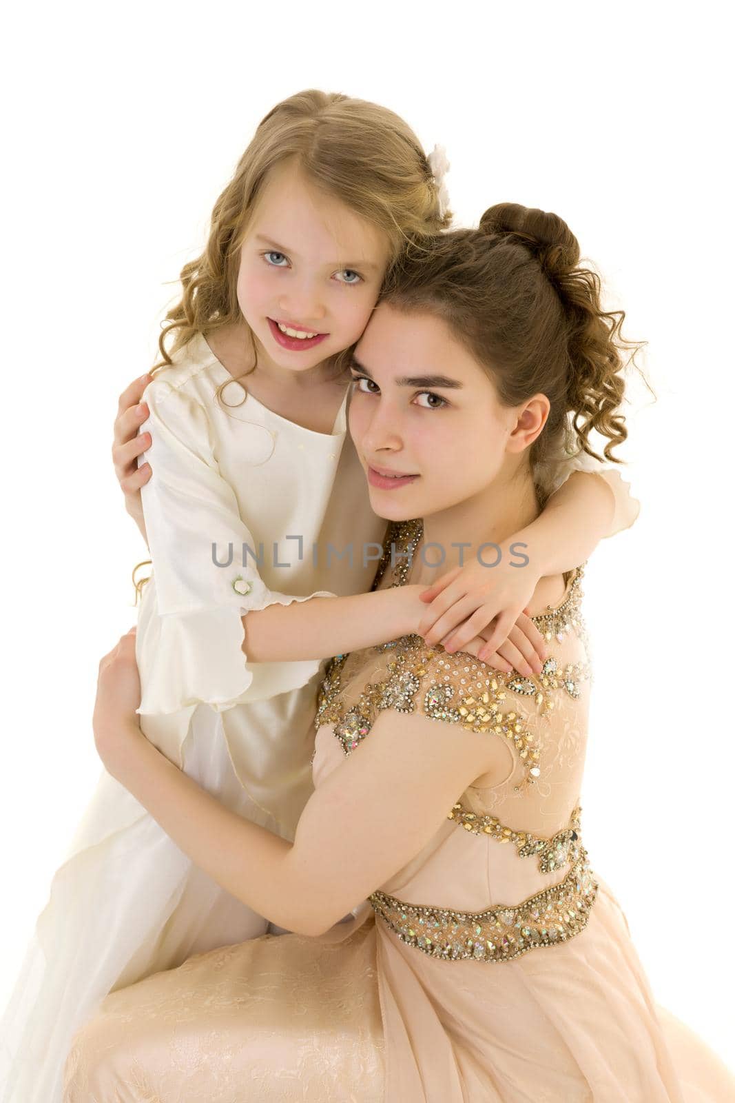 Beautiful young girl hugging her little sister. The concept of a happy childhood, family values. Isolated on white background.