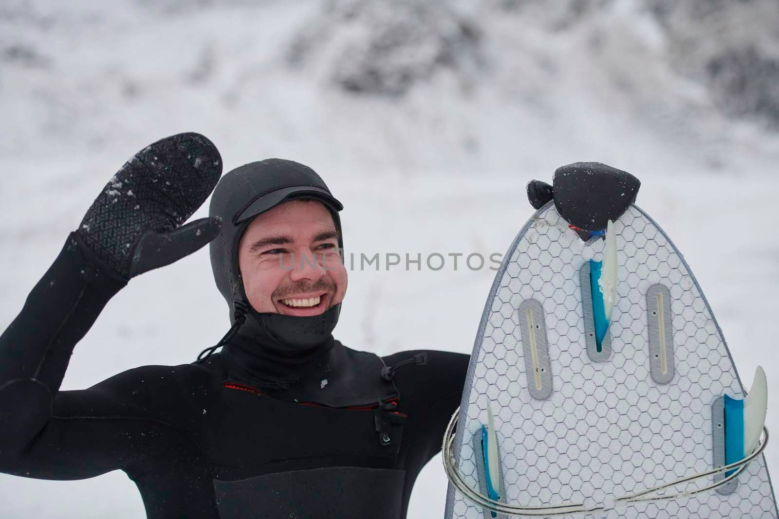 Authentic local Arctic surfer portrait holding a board after surfing in Norwegian sea. Snow capped mountain background. Winter water activities extreme sport