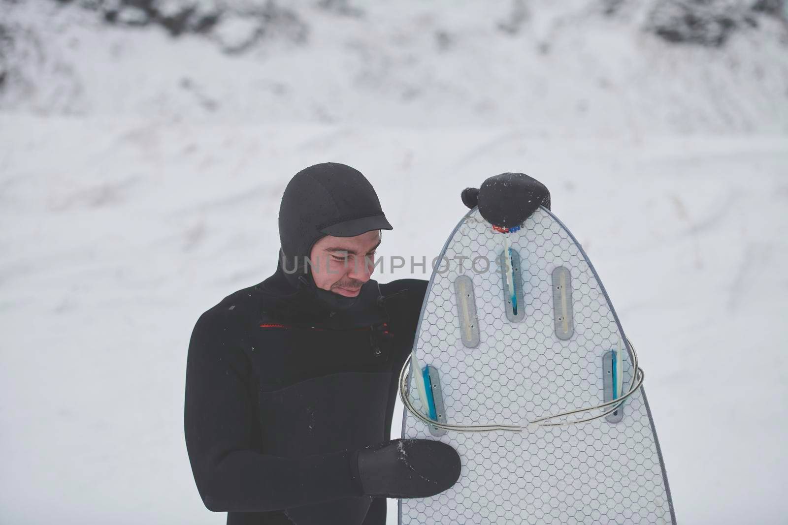 Authentic local Arctic surfer portrait holding a board after surfing in Norwegian sea. Snow capped mountain background. Winter water activities extreme sport