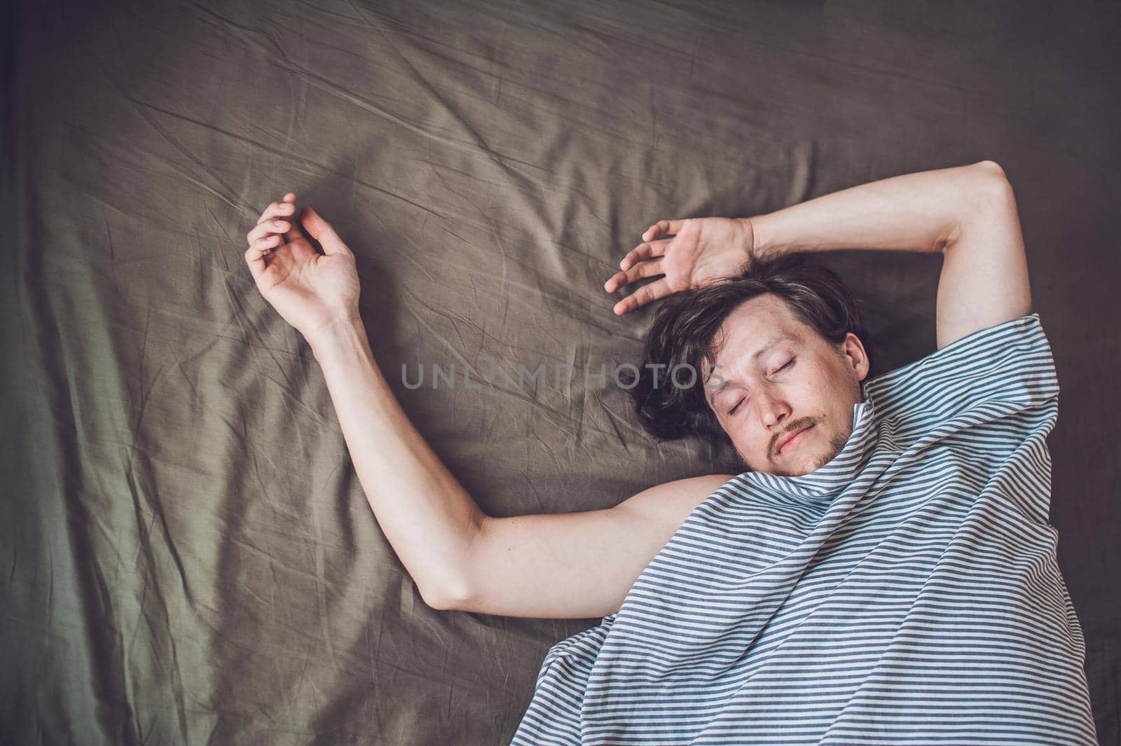 Beautiful young man lying down in bed and sleeping, top view. Do not get enough sleep concept.