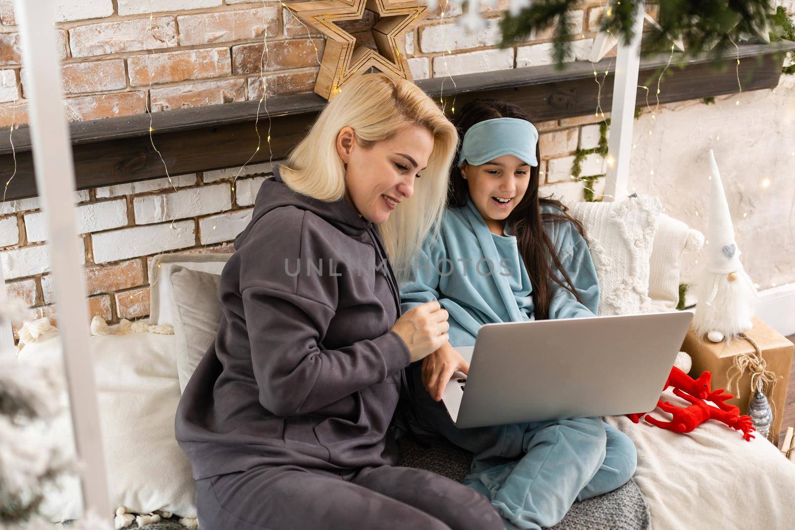 Caucasian woman with her daughter at christmas, having video chat with friends and family on laptop screen, sitting on sofa at home embracing. social distancing during covid 19 pandemic at christmas. by Andelov13