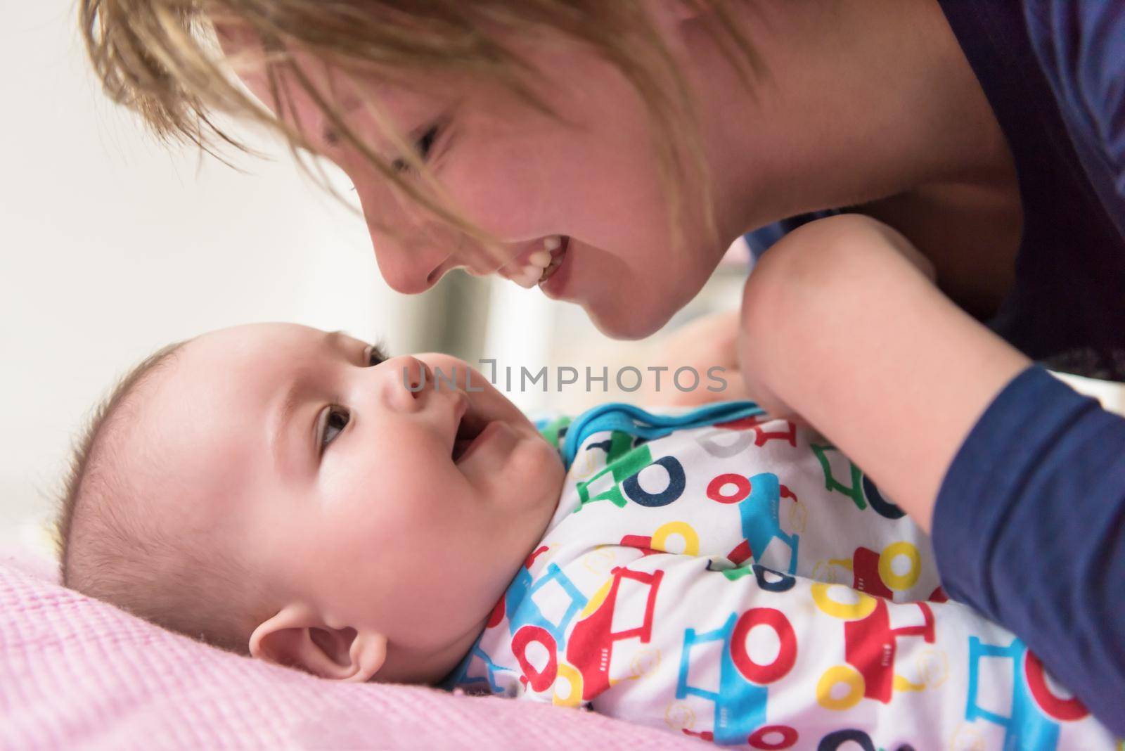 Happy young mother kissing her cute little baby while playing first games on the pink bed at home