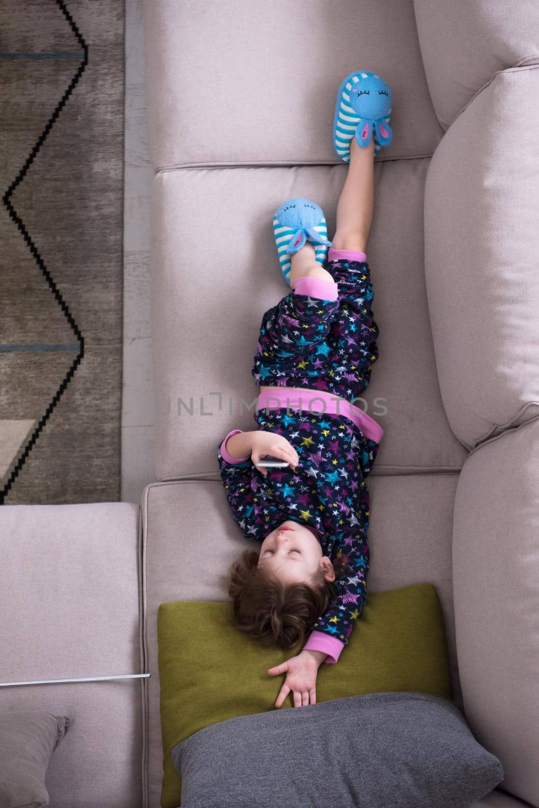 top view of cute little girl using a smartphone and smiling while lying on the sofa at home