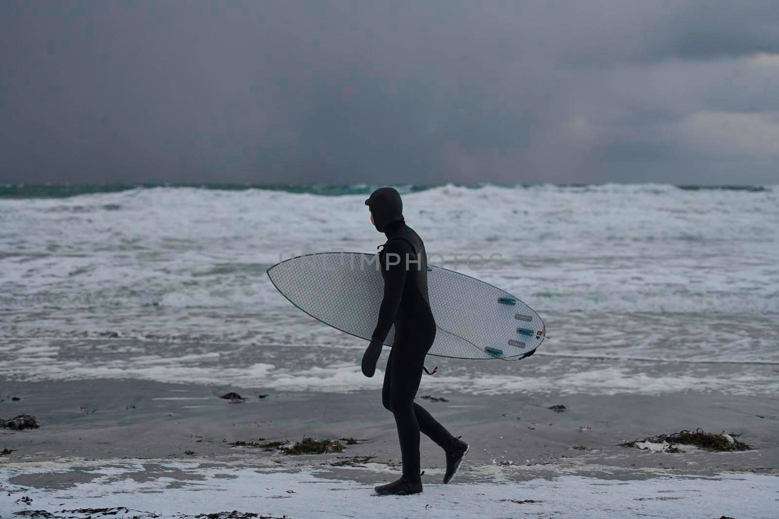 Authentic local Arctic surfer going by beach after surfing in Northern sea. Norwegian sea coastline. Winter water activities extreme sport