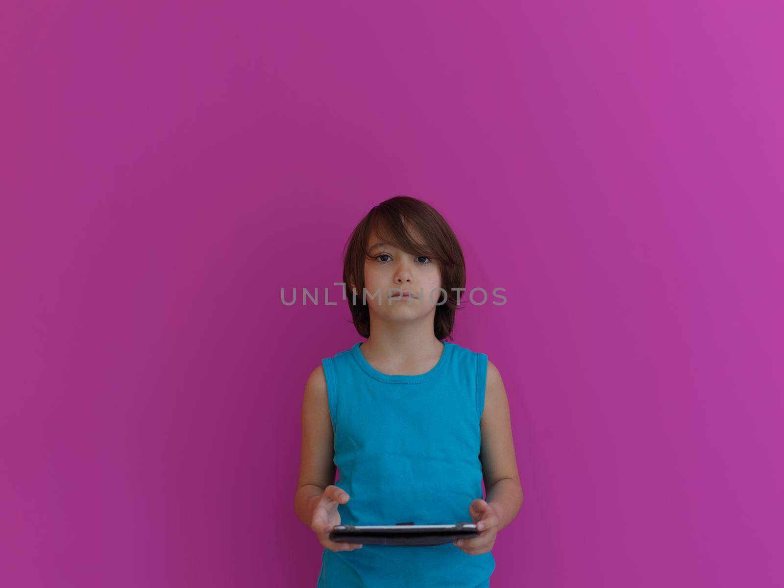 Little Arabian boy sitting using  on digital tablet. Portrait of a young arab child at home watching cartoon with pink background . Modern kid and online education elearning technology.