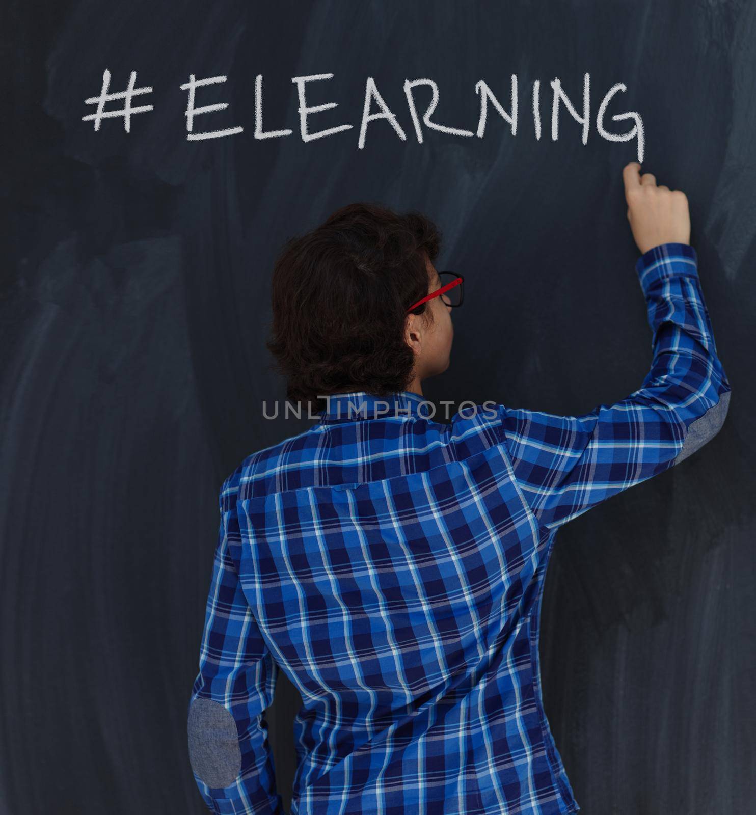 Teen Boy with chalk  writing on black chalkboard hashtag elearning by dotshock