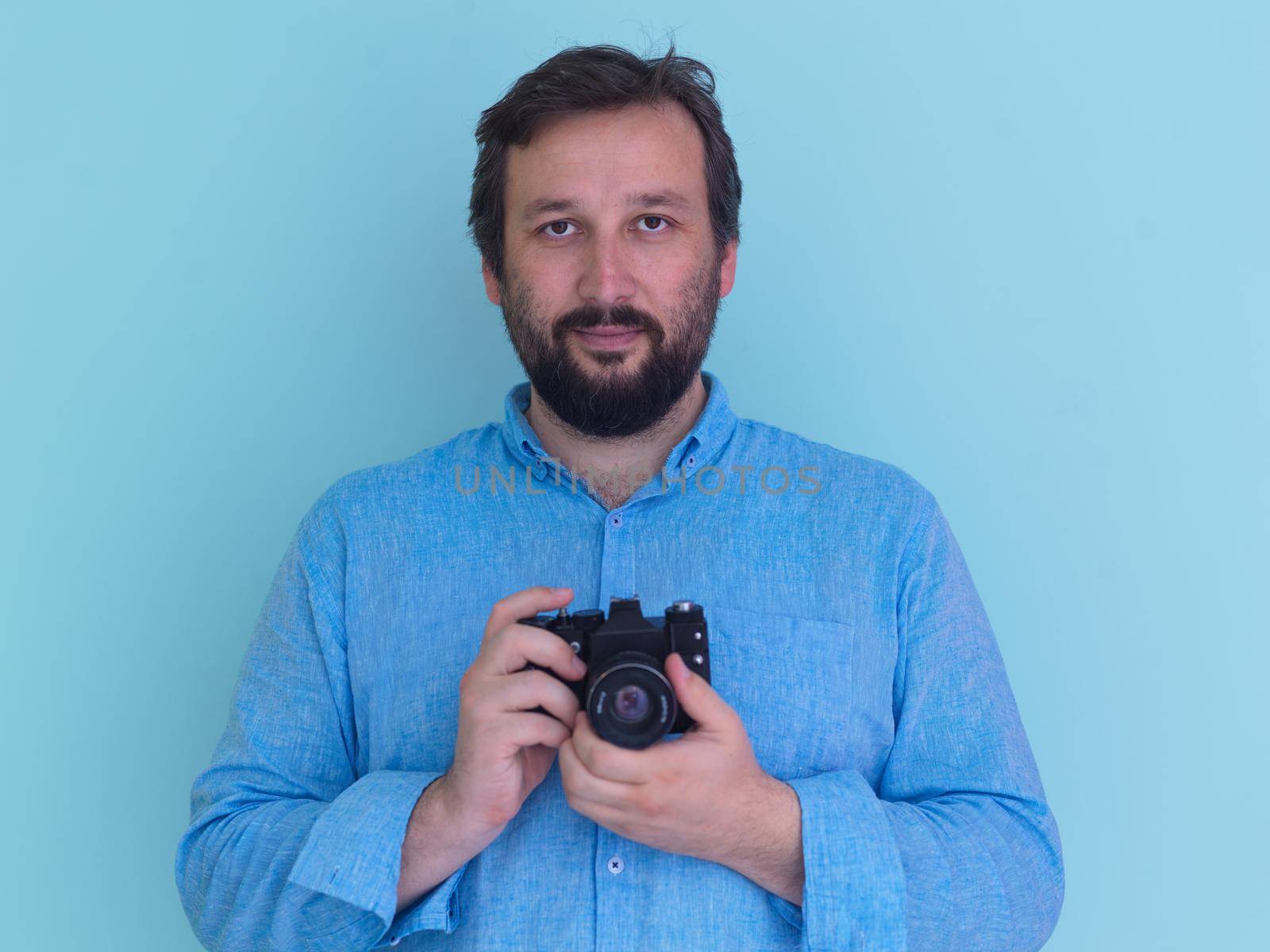 Portrait of  male Photographer in blue shirt holding old analog slr art camera while standing against cyan background