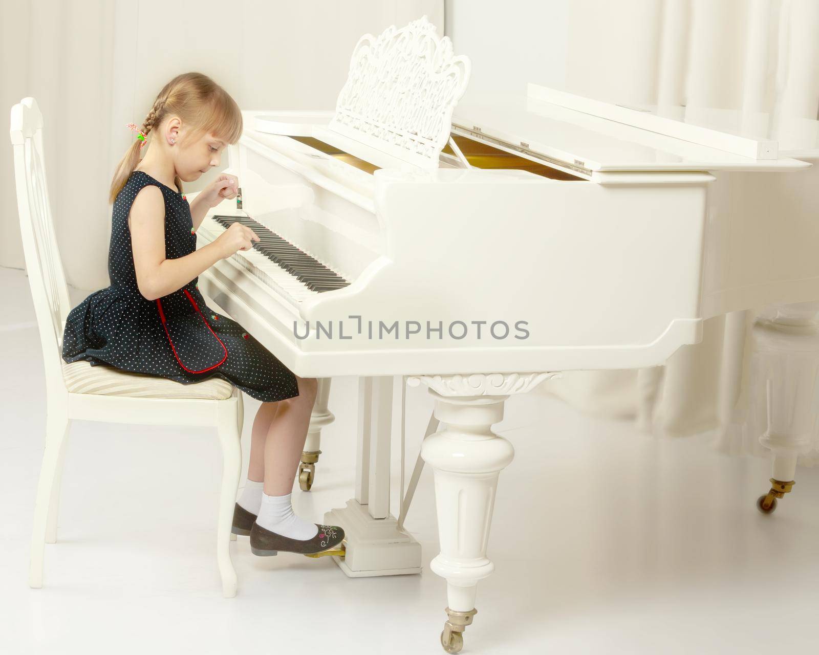 Beautiful little girl is playing on a white grand piano. by kolesnikov_studio